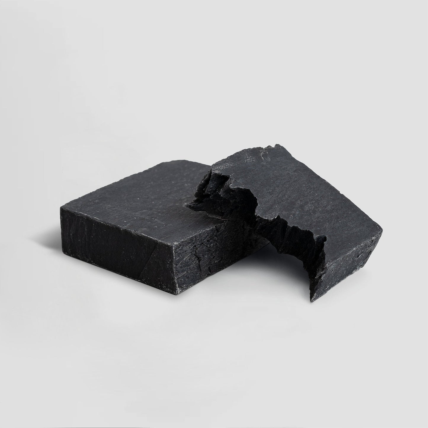 Two pieces of black soap on a light gray background