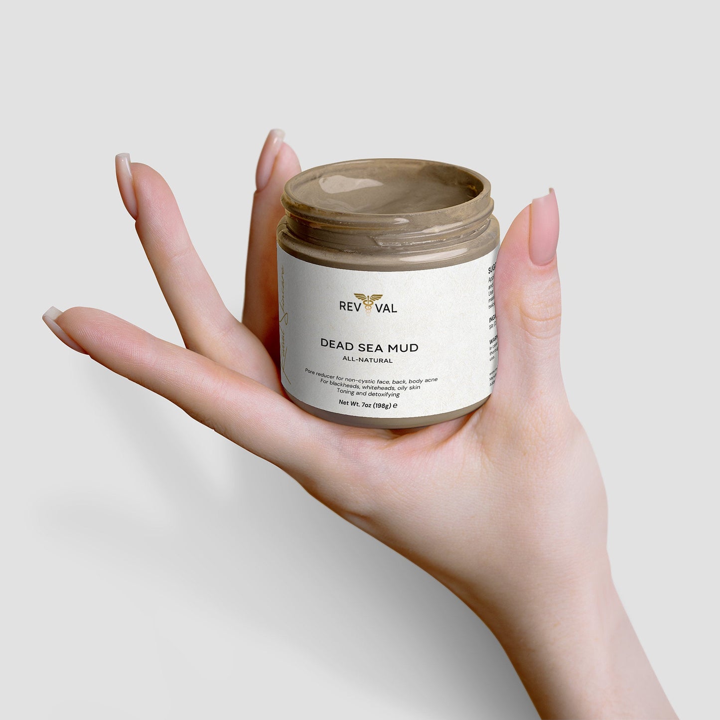 Hand holding a jar of Revival Dead Sea Mud on a light background