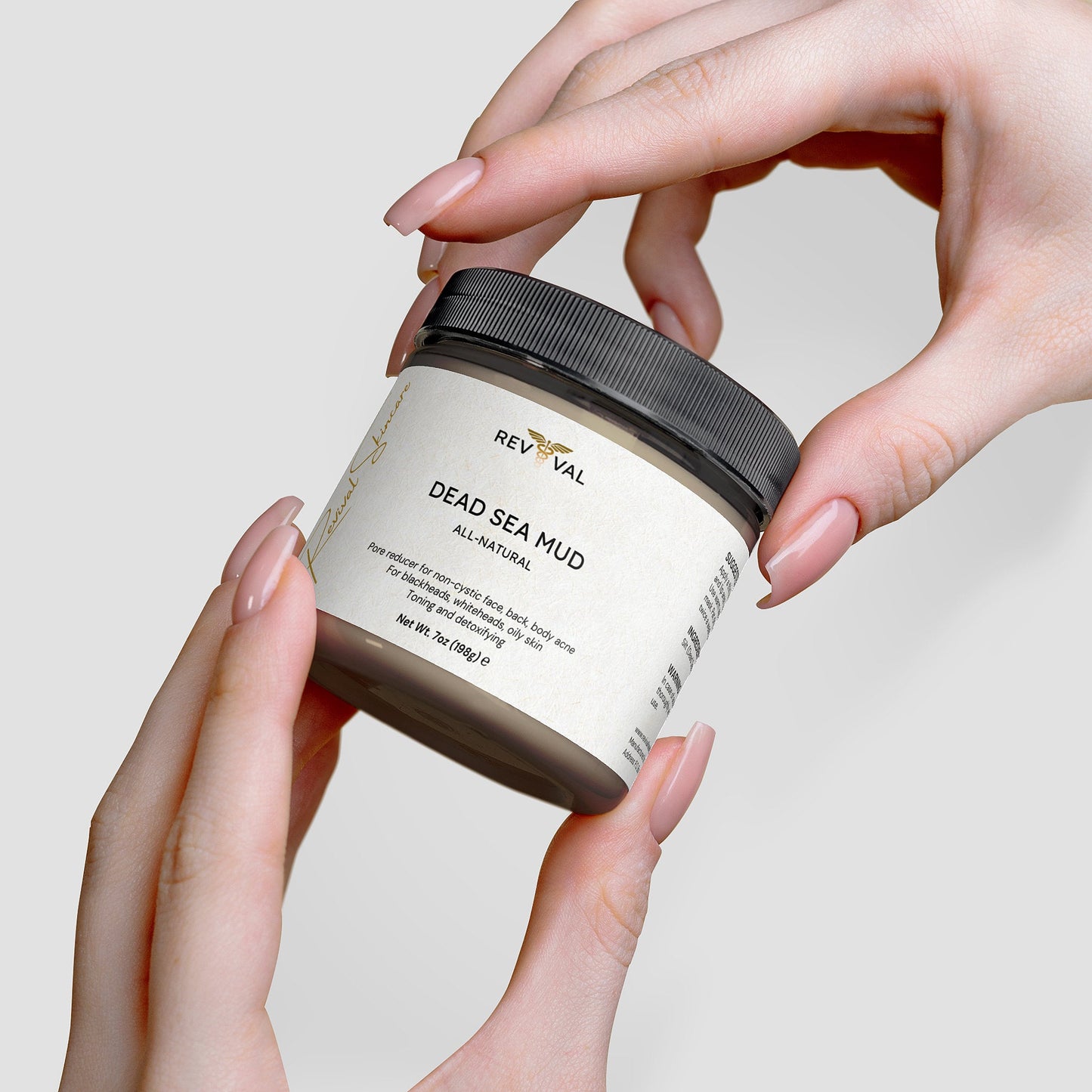 Jar of Reviva Dead Sea Mud held by hands against a neutral background