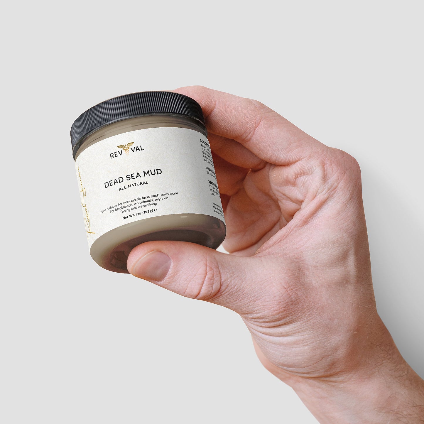 Hand holding a jar of Rev Val Dead Sea Mud on a light background
