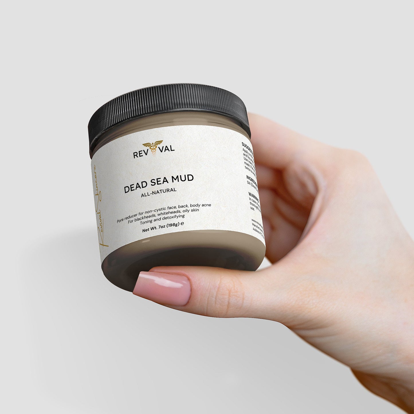 Hand holding a jar of Revival Dead Sea Mud on a light gray background