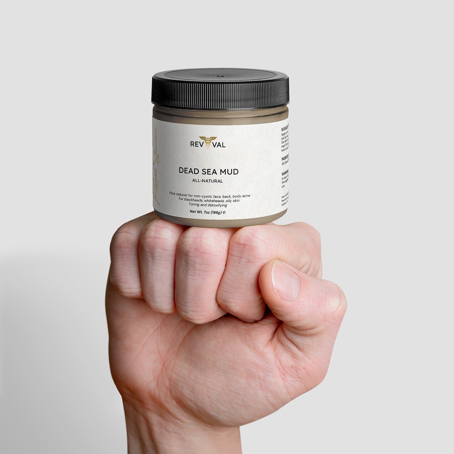 Hand holding a jar of Revival Dead Sea Mud against a light gray background