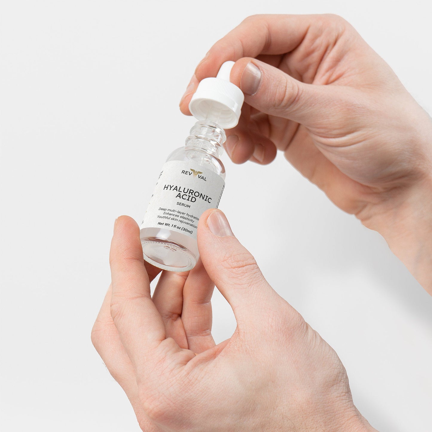 Hand holding a bottle of RevivaL Hyaluronic Acid Serum against a light gray background
