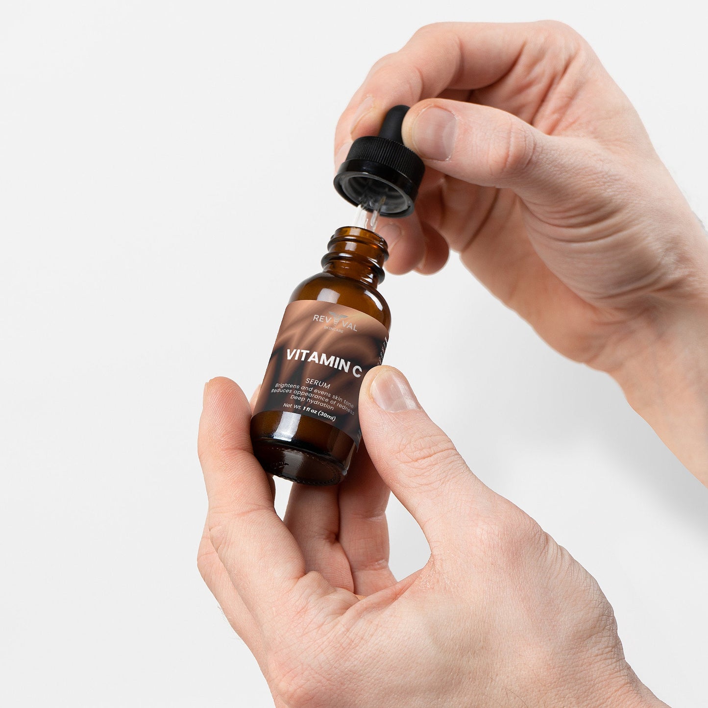 Hand holding a bottle of vitamin C serum with a dropper against a white background