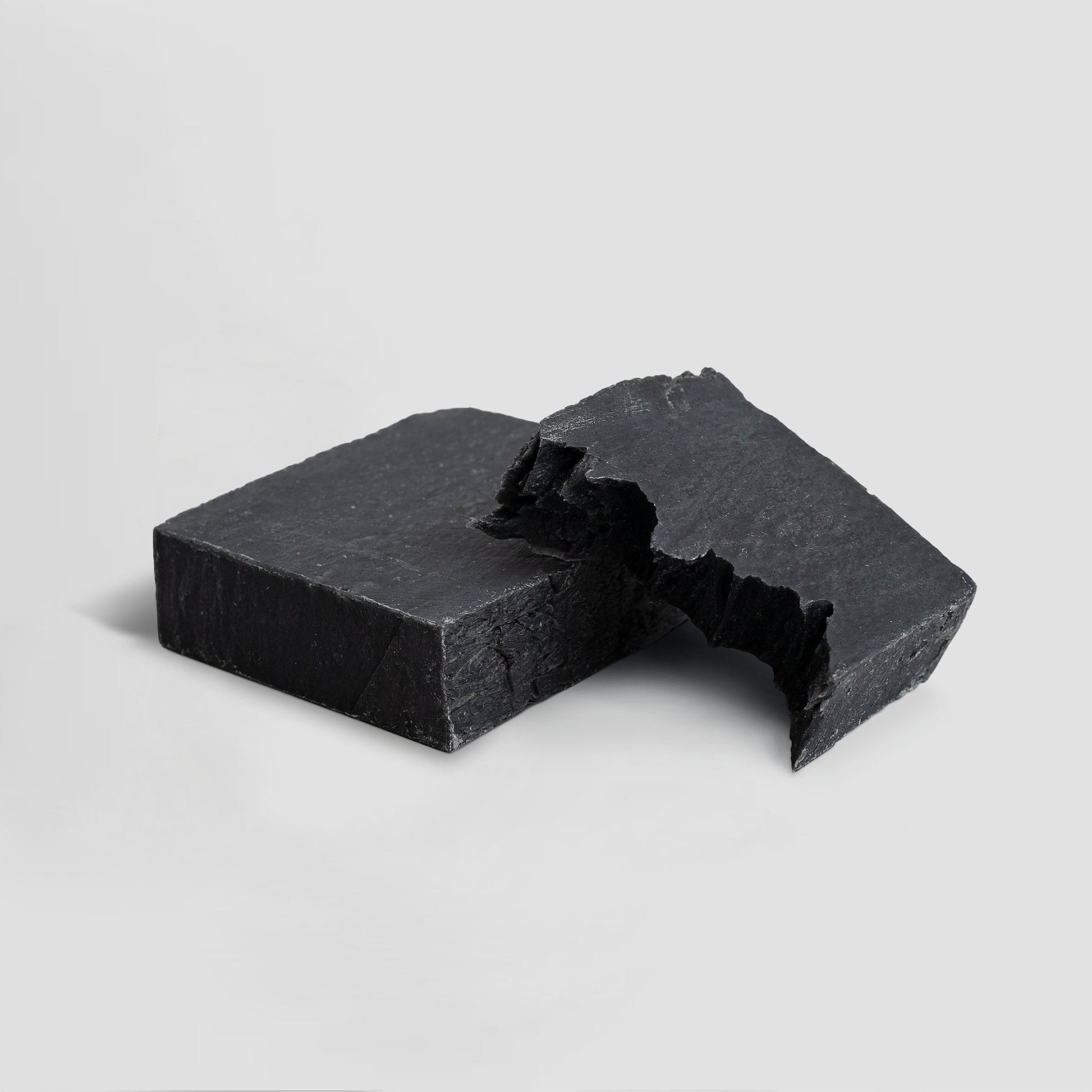 Two pieces of black soap on a light gray background