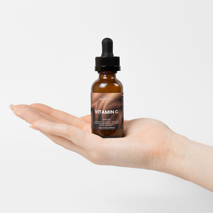 Hand holding a bottle of vitamin C serum against a light background