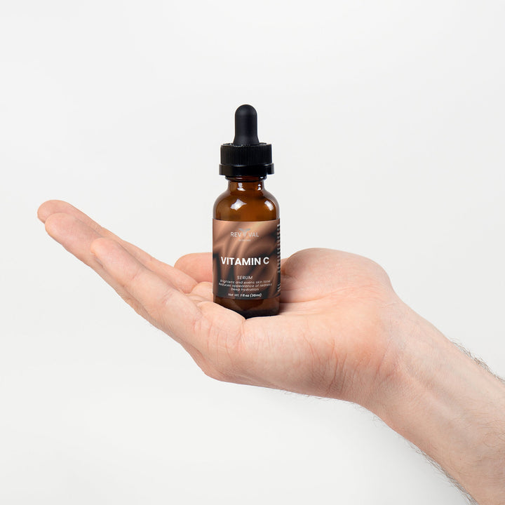 Hand holding a bottle of Vitamin C serum with a dropper against a white background